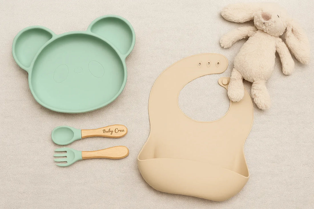 Set repas bébé pastel avec assiette panda en silicone, couverts bois et silicone gravés, bavoir beige et doudou lapin sur fond naturel.