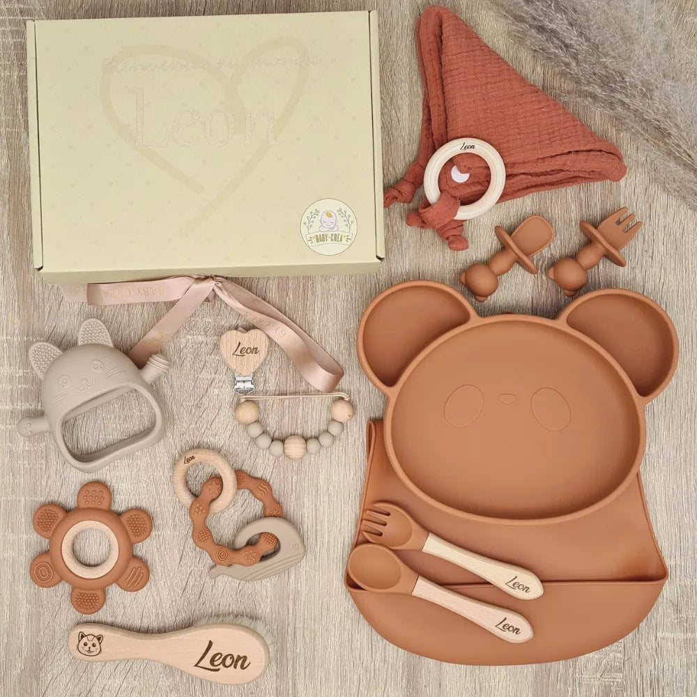 Ensemble d'accessoires de naissance en couleur terracotta comprenant un plateau en forme de panda, des jouets et des couverts, tous portant le nom Léon.