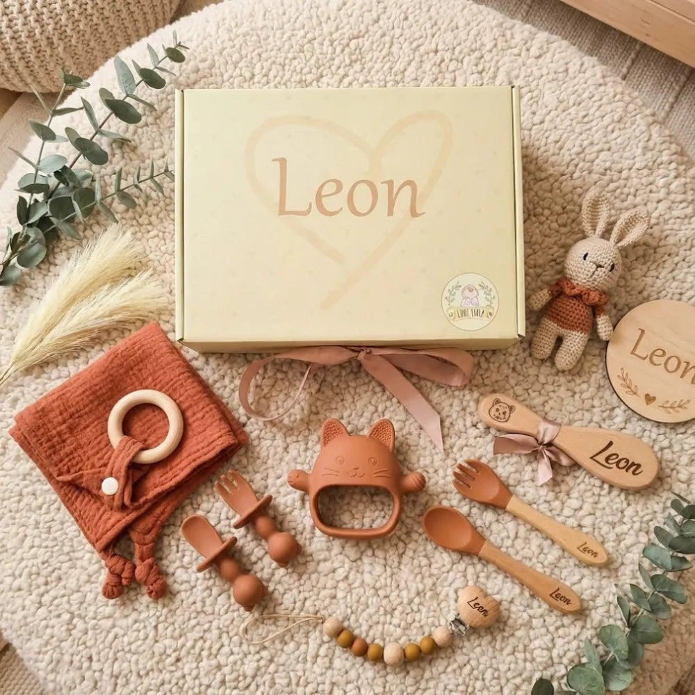 Coffret de naissance d'une douce couleur beige contenant des accessoires pour bébé, incluant des couverts, un jouet et un doudou, personnalisés avec le nom Léon.