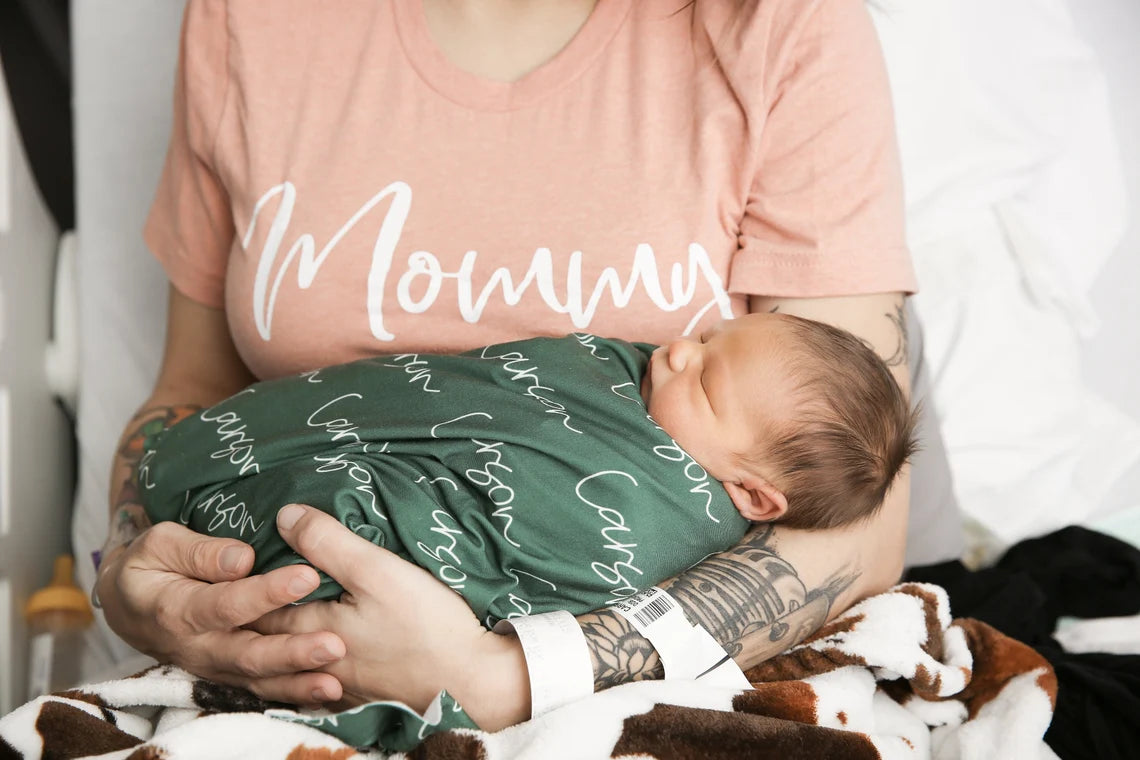 Maman apaisant son nouveau-né grâce à une technique d'emmaillotage avec couverture.