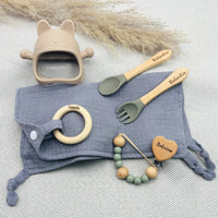 Set repas bébé personnalisé avec bavoir lange gris, couverts en bois gravés Valentin, attache tétine prénom Antoine, anneau de dentition en bois prénom Camille, jouet de dentition chat en silicone beige – cadeau de naissance original et pratique.