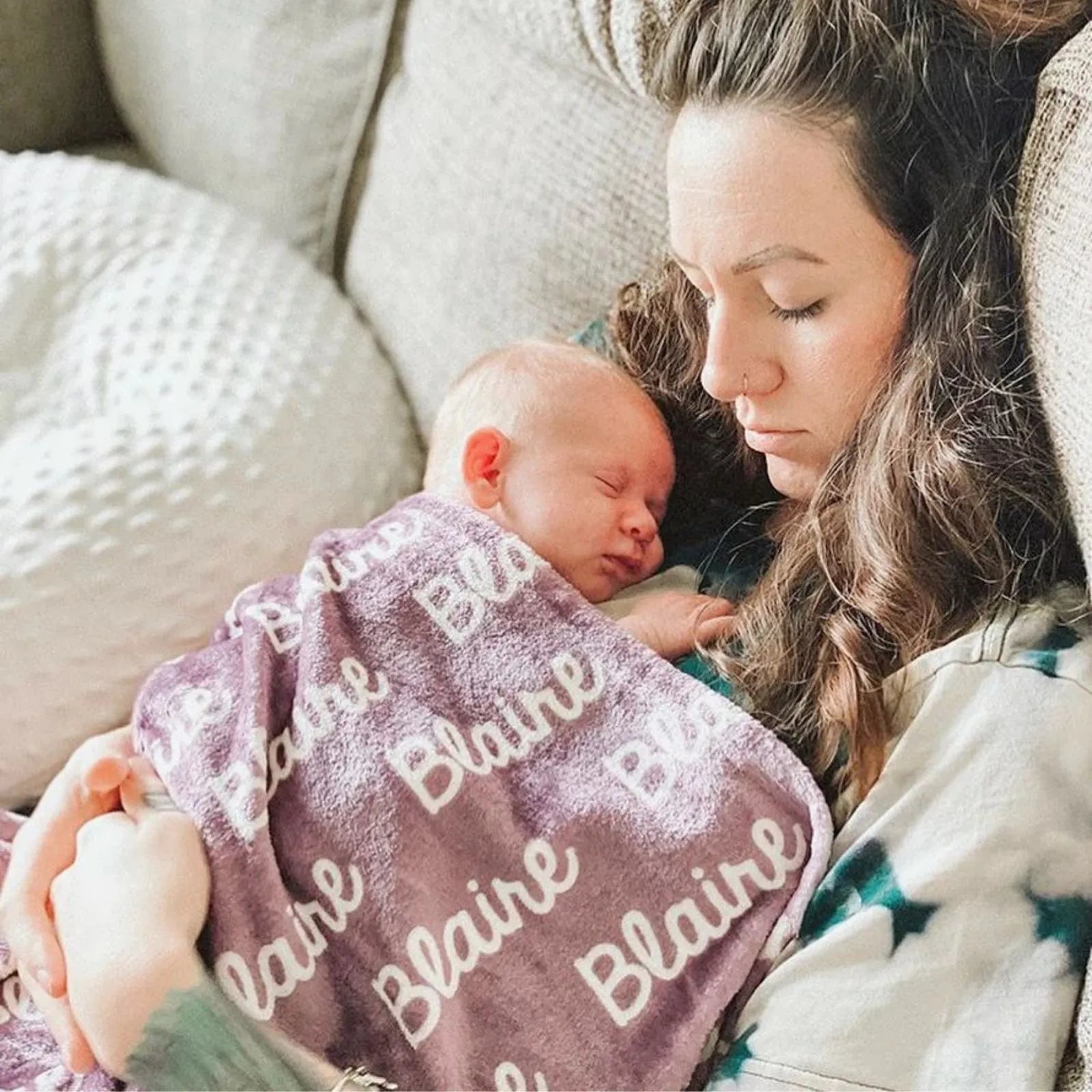 Moment tendresse : Maman tenant son bébé endormi dans un plaid personnalisé mauve prénom Blaine. Couverture polaire douce pour le peau à peau et l'allaitement.