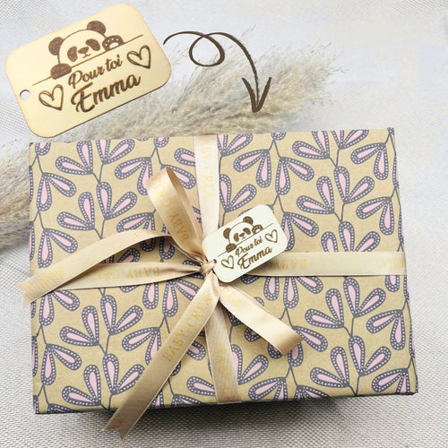 Cadeau de naissance personnalisé pour bébé fille, emballé avec soin dans un papier fleuri beige et rose, ruban satiné BABY-CREA et étiquette gravée au prénom "Emma". Idéal pour un coffret naissance élégant, prêt à offrir dès la maternité.